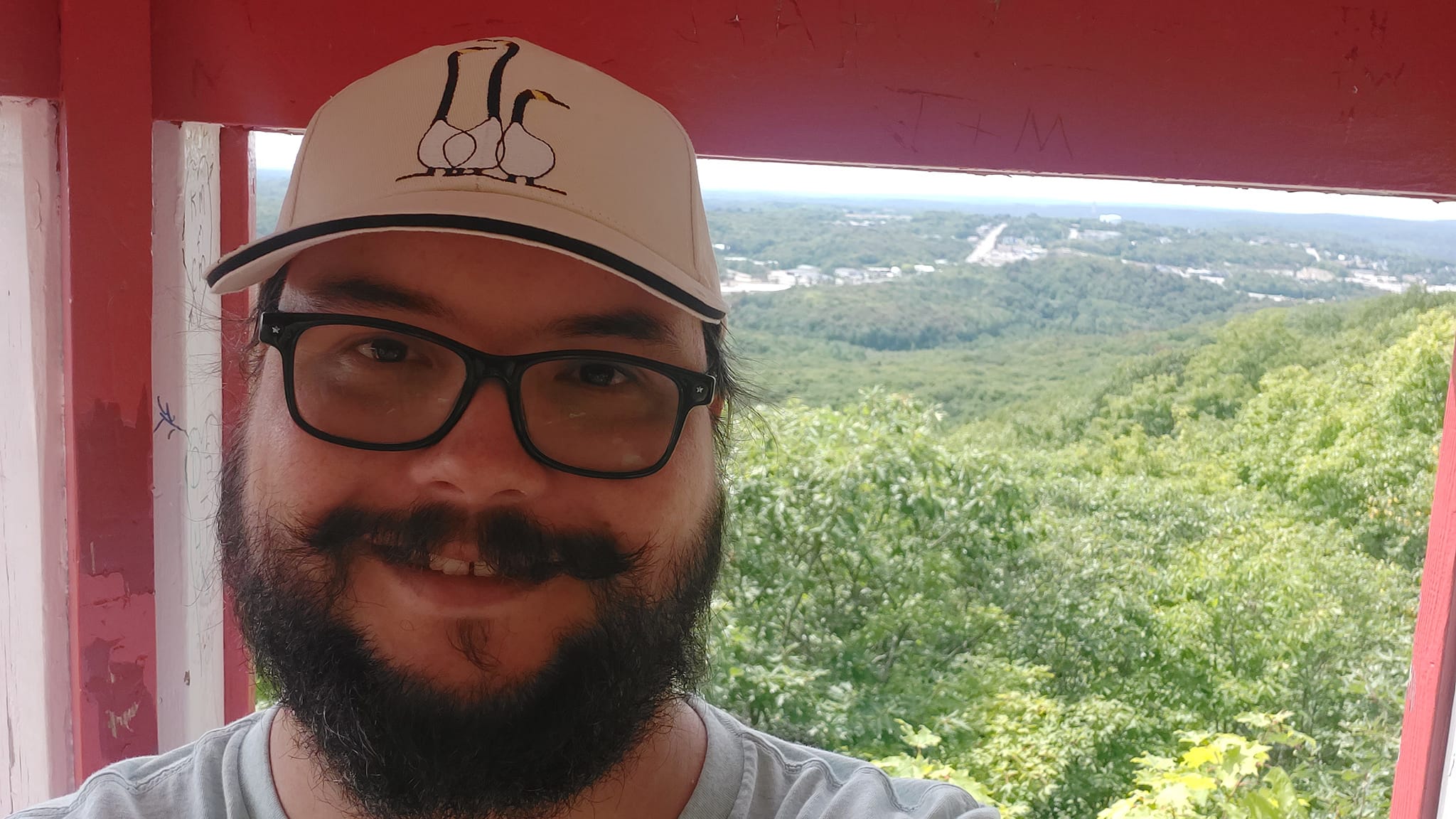 A man short hair and bushy facial hair stands in a lookout structure looking over Elliot Lake